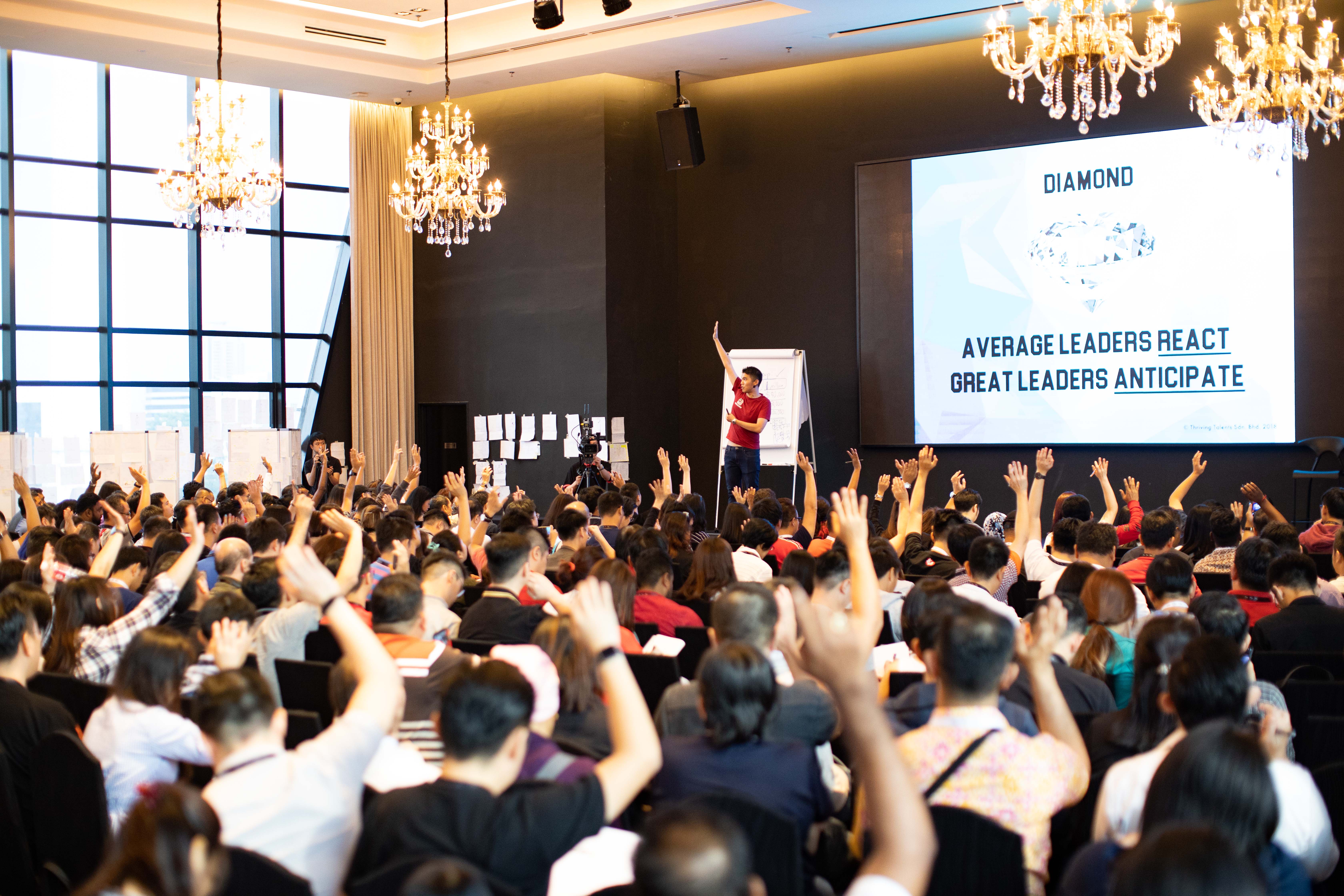 Audience with hands raised at a Michael Teoh leadership session